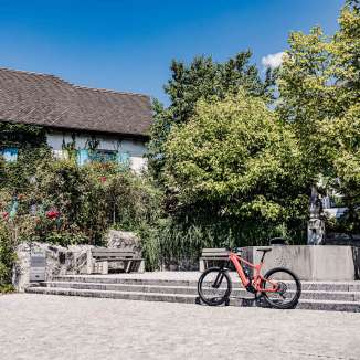 Rode e-bike voor een historisch gebouw in Liechtenstein, omringd door bomen en fonteinen, ideaal startpunt voor een fietstocht door het land