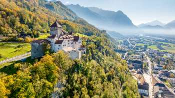 Uitzicht op Kasteel Vaduz met herfstkleurig bos en de stad Vaduz in het dal.