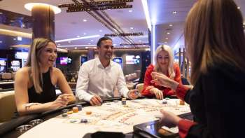 Vriendelijke sfeer aan de speeltafel: drie gasten maken een praatje met de croupière in het stijlvol ingerichte Casino Schaanwald.