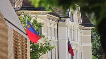 Gezicht op de gevel van het regeringsgebouw in Vaduz met de vlaggen van Liechtenstein op de voorgrond.