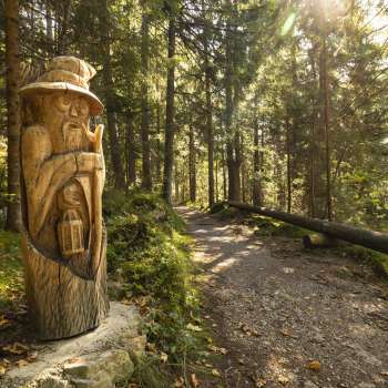Houten figuur met lantaarn op "pad van de Walser legendes" in het mystieke boslicht