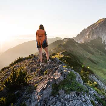 Wandelaar met rugzak staat op een bergkam in Liechtenstein en kijkt in de opkomende zon