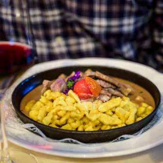 Hartige spätzle met runderragout, gegarneerd met tomaat, geserveerd in een pan - vergezeld van een glas rode wijn op een gedekte tafel.