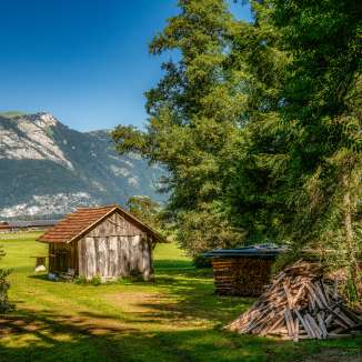Kleine houten schuur op een weiland met een stapel brandhout en uitzicht op de Alpen langs Route 66 in Liechtenstein