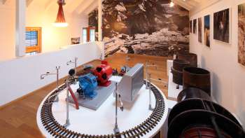 Model van een turbine op een tentoonstellingsplatform in het Lawena Museum, met historische zwart-witfoto's op de achtergrond.