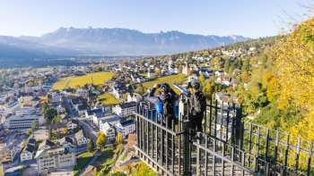 Wandelaars bij de reling van het uitzichtpunt Känzile met panoramisch uitzicht op Vaduz en de omliggende bergen. Wandelaars bij de reling van het uitzichtpunt Känzile met panoramisch uitzicht op Vaduz en de omliggende bergen.