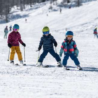 Drie kinderen leren skiën in het Malbun familieskigebied in Liechtenstein bij zonneschijn en poedersneeuw