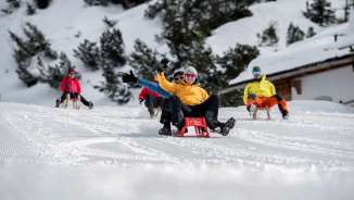 Groep gelukkige rodelaars op een geprepareerde piste in Malbun, omringd door besneeuwde bomen en alpine winterlandschap