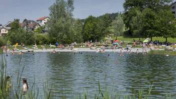 Zomerse zwemdag in de natuurlijke vijver van Recreatiecentrum Grossabünt, omgeven door groene weiden en bomen.