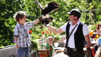 Een jongen houdt een roofvogel in zijn armen, geleid door een valkenier in traditionele kleding, tijdens een roofvogeldemonstratie in Malbun