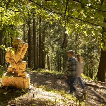 Wandelaars passeren een gebeeldhouwde figuur met verrekijker op "pad van de Walser legendes".