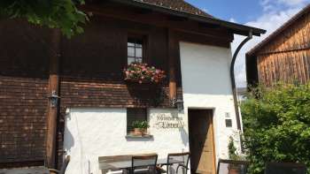 Rustieke herberg met houten gevel en ramen versierd met bloemen, omgeven door groene natuur