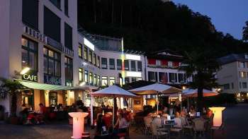 Avondsfeer voor Brasserie Burg in Vaduz met verlicht terras en gasten onder parasols.