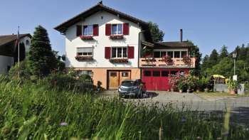 Charmant buitenaanzicht van de Bed & Breakfast Büchel met rode luiken en bloemenweide op de voorgrond.