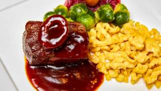 Heerlijke wildschotel met donkere saus, goudgele spätzle, spruitjes en veenbessen geserveerd op een wit bord.
