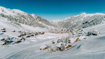 Luchtfoto van Malbun in de winter met besneeuwde houten huizen, genesteld in het Liechtensteinse Alpenlandschap