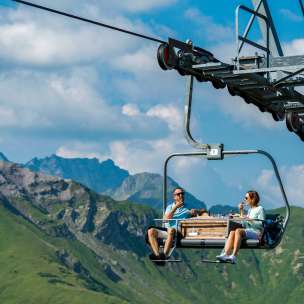 Twee personen genieten van een ontbijt op de plezierstoeltjeslift in Malbun met een indrukwekkend bergdecor op de achtergrond