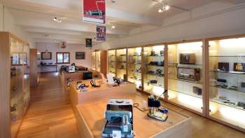 Uitzicht in een lichte tentoonstellingsruimte van het Lawena Museum met verlichte vitrines vol historische elektrische apparaten. Uitzicht in een lichte tentoonstellingsruimte van het Lawena Museum met verlichte vitrines vol historische elektrische apparaten.