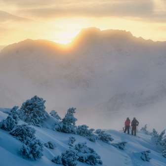 Twee personen, waaronder Tina Weirather, wandelen bij zonsondergang door een besneeuwd winterlandschap in de bergen van Liechtenstein.