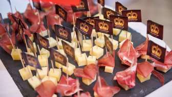 Voorgerechten met blokjes kaas en luchtgedroogde ham, versierd met individueel bedrukte merkvlaggen op een leistenen bord