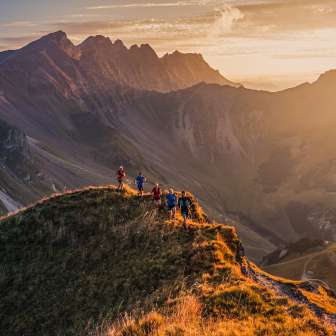 Groep trailrunners op een bergkam bij Malbun, Liechtenstein, in het warme licht van de zonsondergang met uitzicht op de Alpen