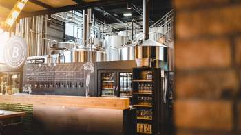 Binnenzicht van een brouwerij met roestvrij stalen brouwsysteem en uitnodigende bar op de voorgrond.