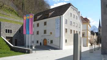 Buitenaanzicht van het Nationaal Museum van Liechtenstein in Vaduz met kleurrijke vlaggen en een blik op de historische gevel.