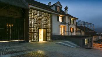 Modern verlicht Kulturhaus Rössle in Mauren bij schemering, met glazen gevel, historische gebouwuitbreiding en geplaveid voorplein.