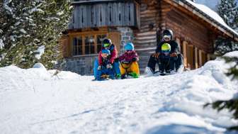 Rodelen met kinderen in Malbun Twee volwassenen en drie kinderen zitten op sleeën en beginnen samen aan een afdaling voor een besneeuwde berghut in Malbun