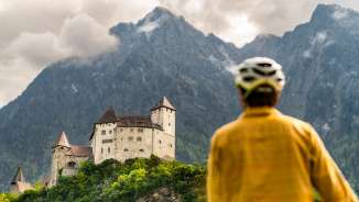 Fietser met helm bekijkt het imposante burcht Gutenburg tegen een dramatisch bergdecor in Balzers - culturele fietstocht in Liechtenstein