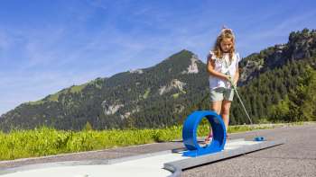 Meisje concentreert zich op een blauwe loopingbaan in een alpine omgeving tijdens het minigolfen