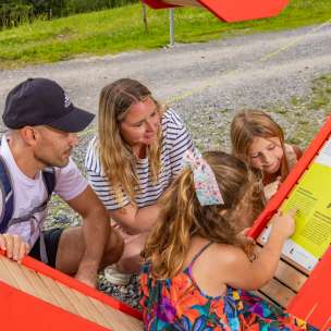 Een gezin met kinderen leest gretig het informatiebord op pad van het Alpijns hart in Malbun, een interactieve wandelroute in de bergen van Liechtenstein.