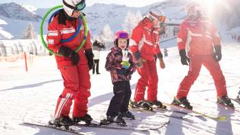 Drie skileraren in rode pakken en een kind op ski's in de sneeuw, besneeuwde bergen en zonneschijn op de achtergrond
