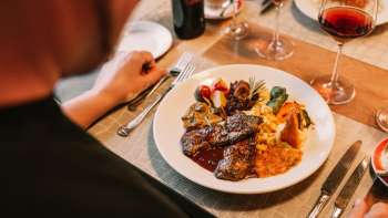 Close-up van een hoofdgerecht met vlees, groenten en fijne sauzen, vergezeld van rode wijn