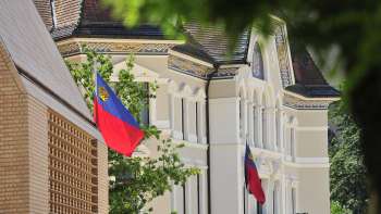 Gezicht op de gevel van het regeringsgebouw in Vaduz met de vlaggen van Liechtenstein op de voorgrond.