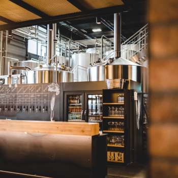 Binnenzicht van een brouwerij met roestvrij stalen brouwsysteem en uitnodigende bar op de voorgrond.
