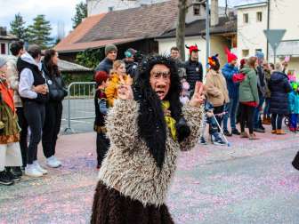 Verklede Schaanse heks bij de carnavalsoptocht in Schaan, voor publiek en kleurrijke confetti op straat