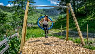 Vrouw schommelt op een nestschommel in Malbun, Liechtenstein, omringd door bergen, weiden en zomerse natuur