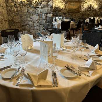 Elegant gedekte ronde tafel met witte tafelkleden, servetten en menu's voor een stenen muur.