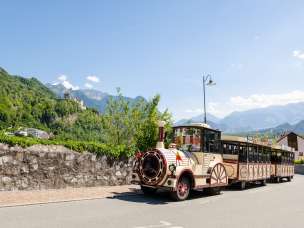 Citytrain rijdt door Vaduz, op de achtergrond het kasteel van Vaduz en de Alpen in de felle zon
