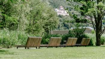Rustige ligweide met houten ligstoelen in natuurpark Haberfeld, met uitzicht op het kasteel op de achtergrond.