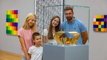 Gezin met twee kinderen kijken naar een glazen vitrine met een gouden beeld in het museum