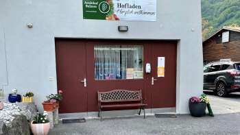 Ingang van de boerderijwinkel Aeulehof met rood hek, bankje en bloemdecoraties in Triesen, Liechtenstein.