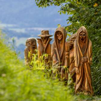 Detailopname van gebeeldhouwde houten figuren in mystieke uitbeelding op het Walser Legendepad in Triesenberg, omgeven door groene natuur