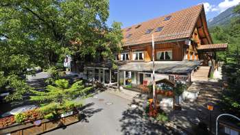 Buitenaanzicht van het hoofdgebouw van camping Mittagsspitze met restaurant en schaduwrijk terras.