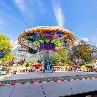 Grote kleurrijke kettingcarrousel op de kermis in Balzers, vol gelukkige bezoekers voor een bergdecor onder een blauwe hemel.