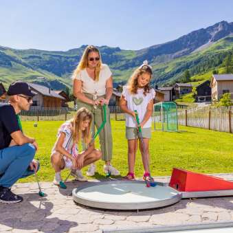 Gezinnen spelen samen minigolf in het zonnige bergdorp Malbun in Liechtenstein - plezier voor jong en oud in de Alpen.