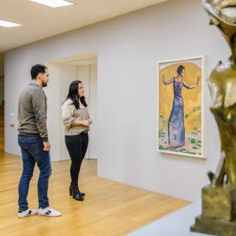 Paar kijkt naar schilderijen in de lichte galerij van het Kunstmuseum Liechtenstein met moderne beeldhouwkunst op de voorgrond.