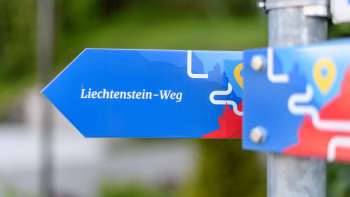 Blauwe wegwijzer met het opschrift "Liechtenstein-Weg" in een modern ontwerp.