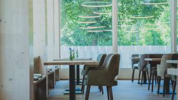 Licht, modern restaurant met houten lambrisering, comfortabele zitplaatsen en grote ramen met uitzicht op het groen